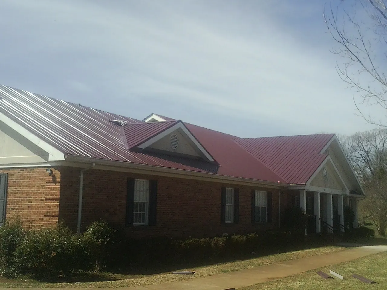 Red metal roof with gabled entries on a long brick building, from a Hail Damage Roof Repair job in Blanchester