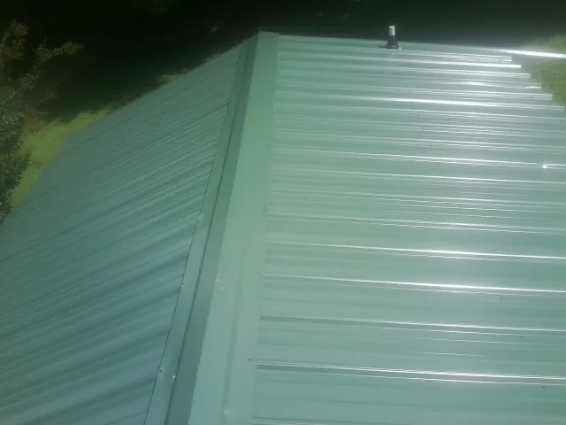 New green metal panels meeting at the ridge of a roof — Flat Roof Repair work by our crew in Blanchester